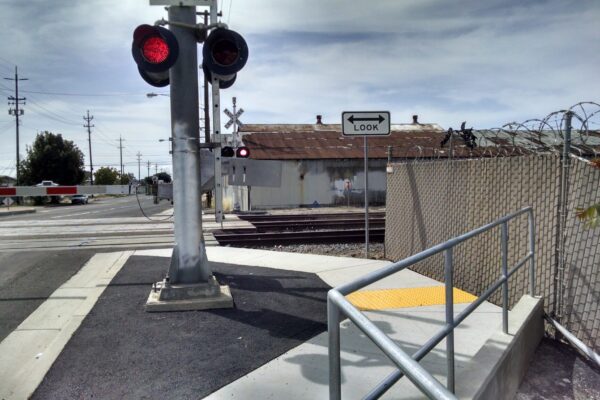 ADA compliant railway crossing. Active railroad crossing guard with lights in front of train tracks.